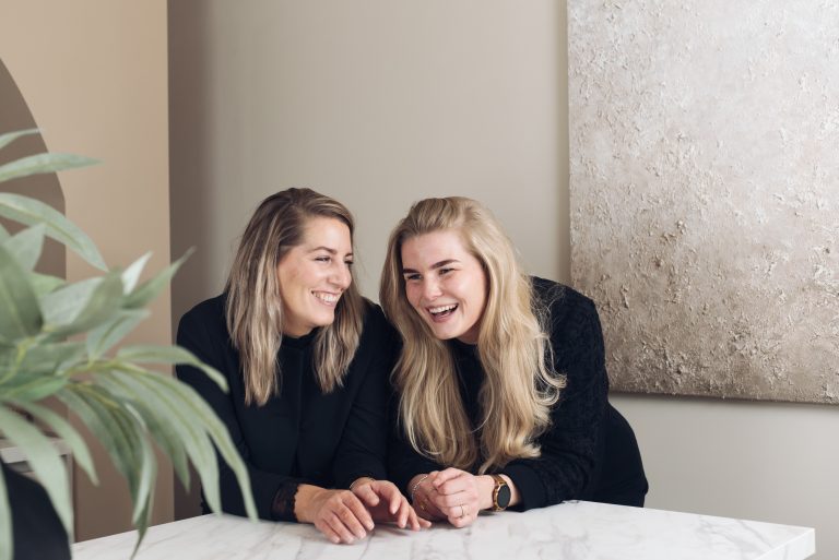 Ontspannen werkplek met twee lachende vrouwen die plezier en werkplezier uitstralen.