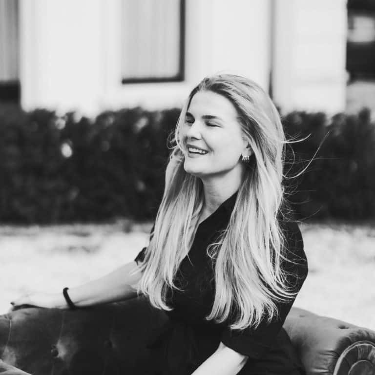 Vrouw met lang blond haar die geniet van werkplezier en groei, zittend op een bank buiten.